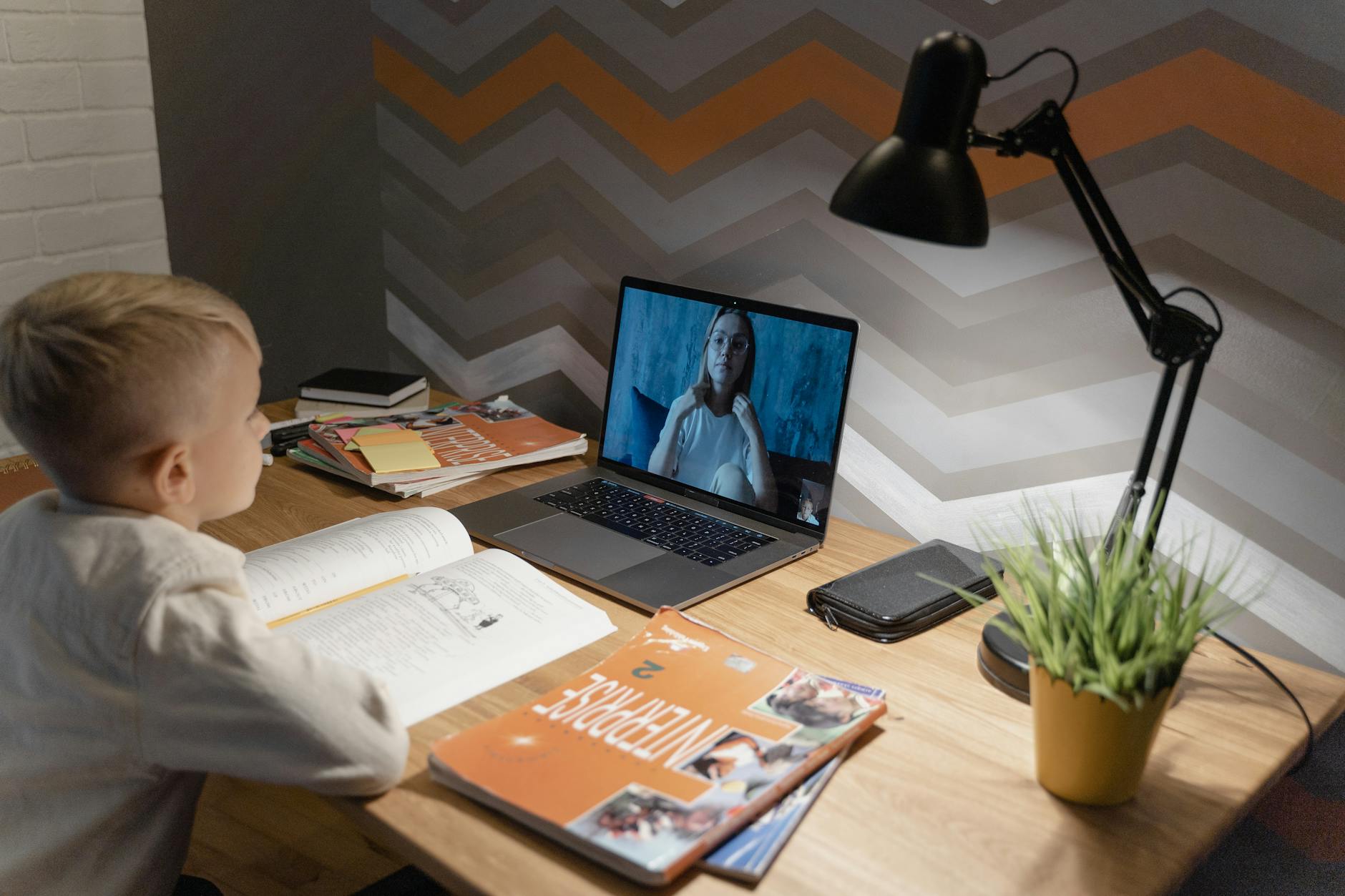 A young boy participates in a virtual class from home, using a laptop and study materials — UPI Study