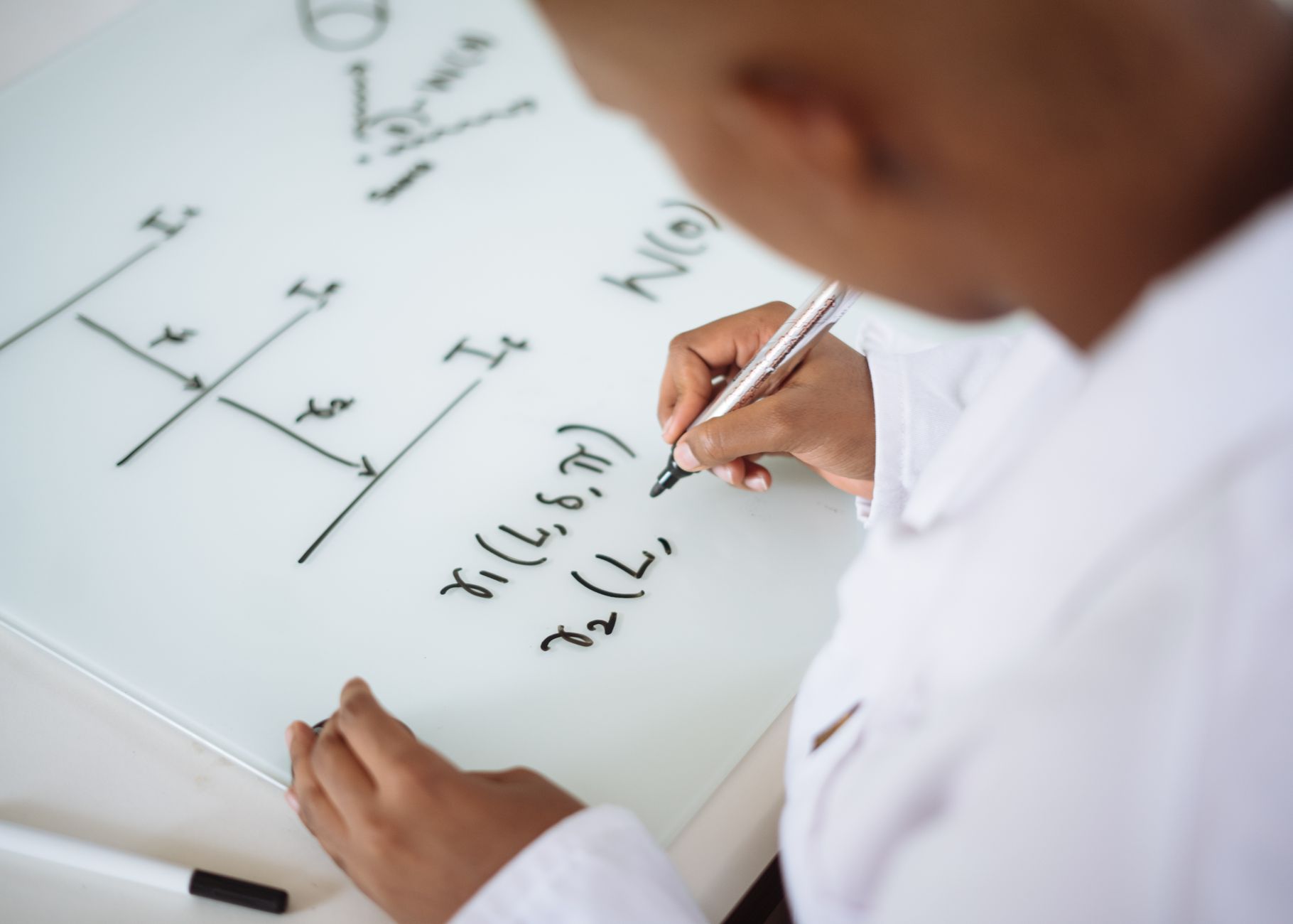From above anonymous ethnic student wearing uniform and solving problem in chemistry while writing formula on white table in lab — UPI Study