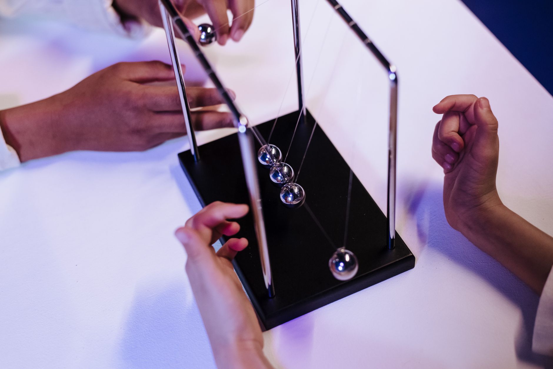 Close-up of hands interacting with a Newton's cradle on a white table in a studio setting — UPI Study