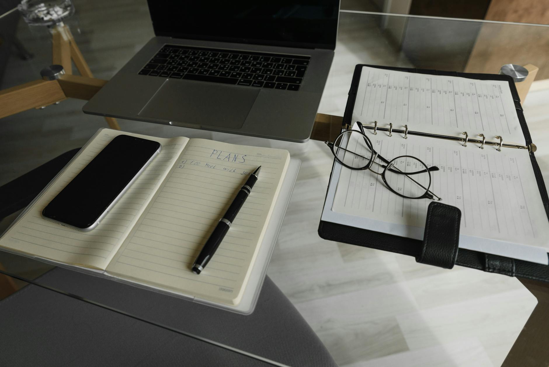 A neatly organized workspace featuring a laptop, smartphone, notebook, pen, and planner on a glass table — UPI Study