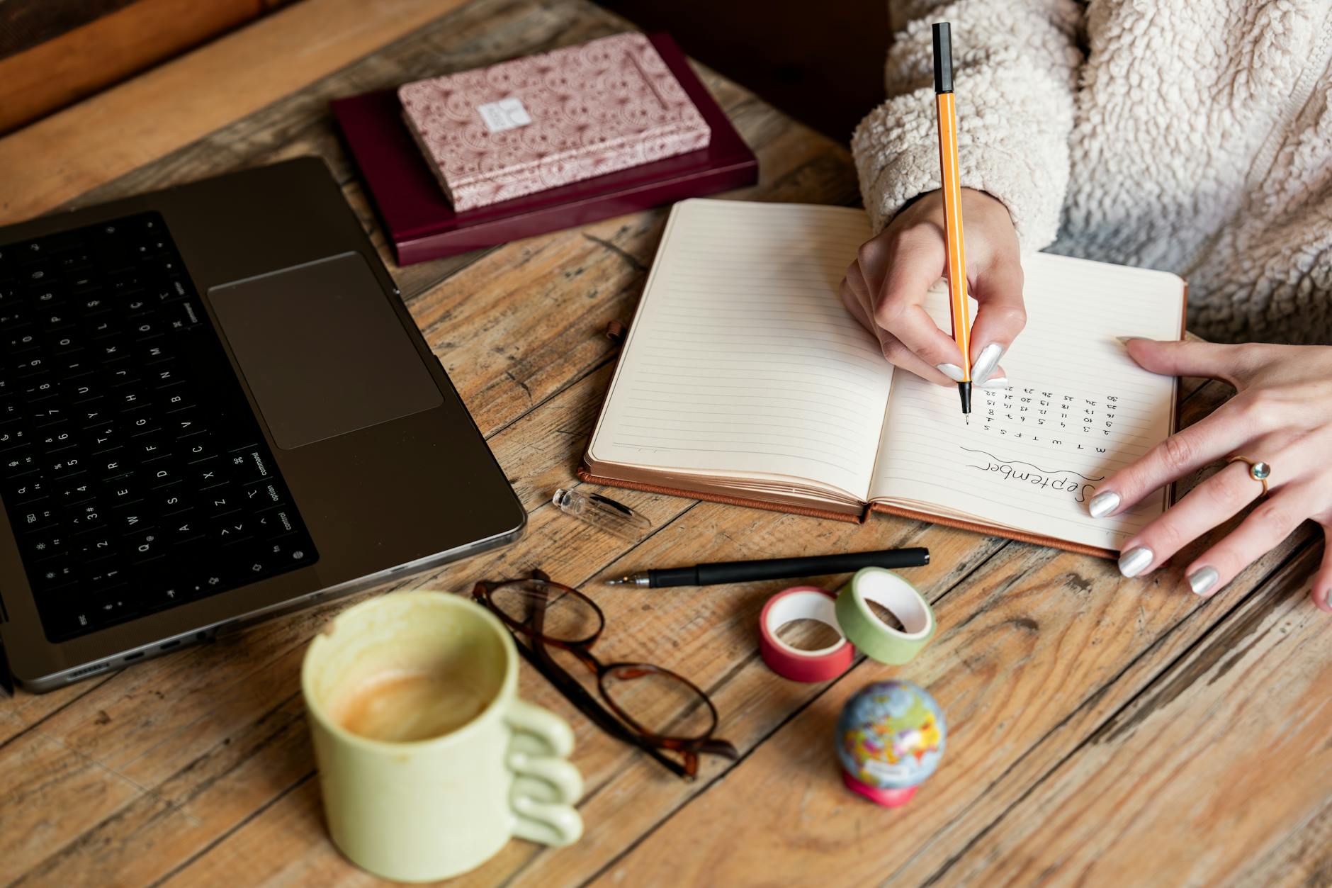 A woman planning her schedule in a notepad beside a laptop and coffee on a wooden desk — UPI Study