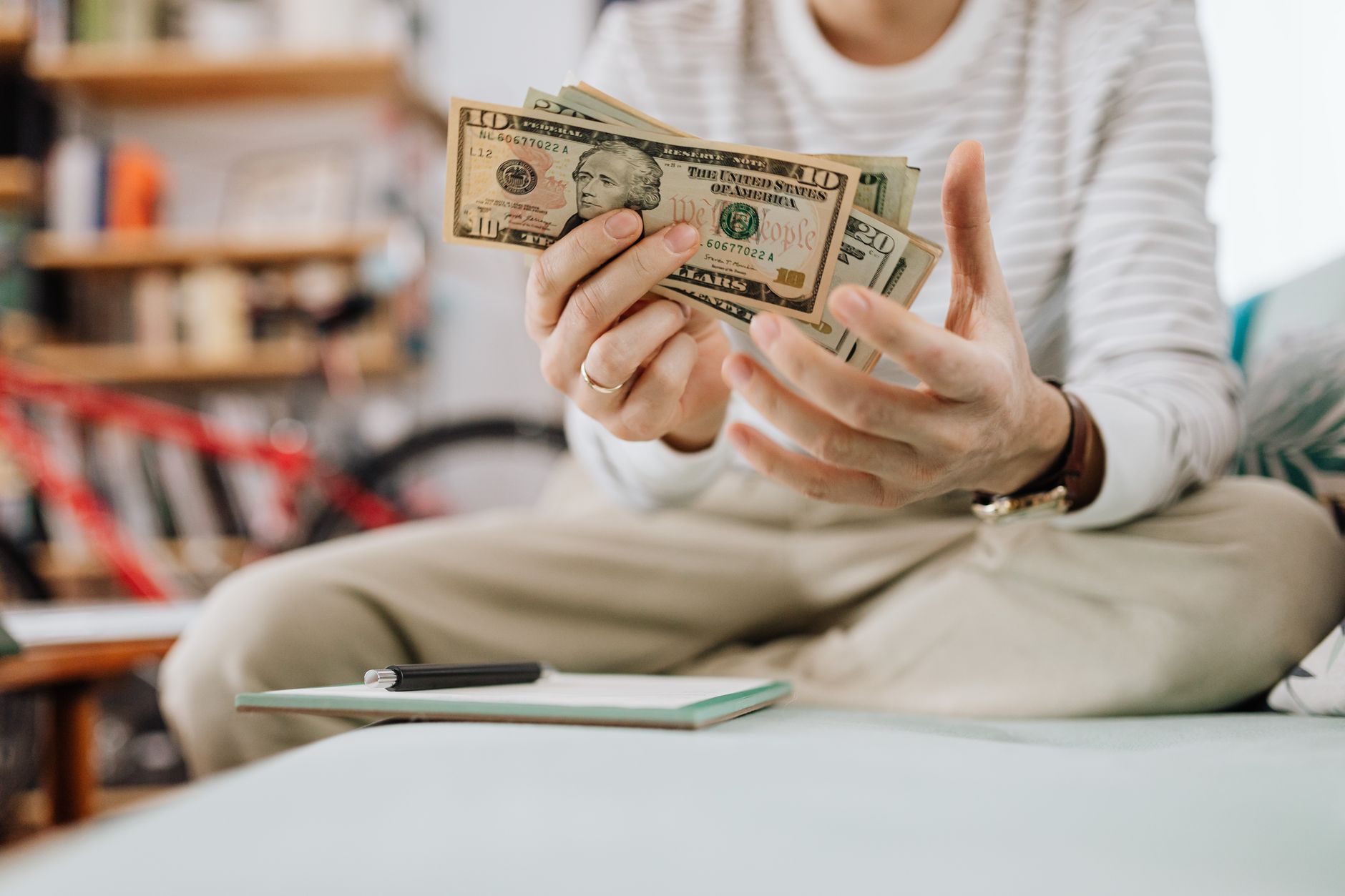 Man wearing casual clothes counts dollar bills while sitting on a sofa indoors — UPI Study