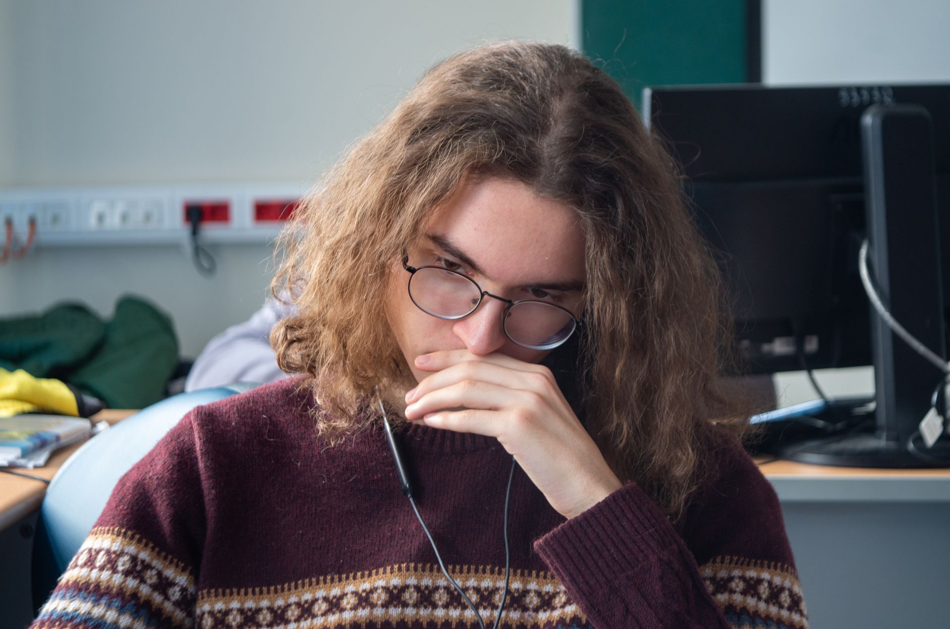 Young adult wearing glasses and sweater, deep in thought at a workstation — UPI Study