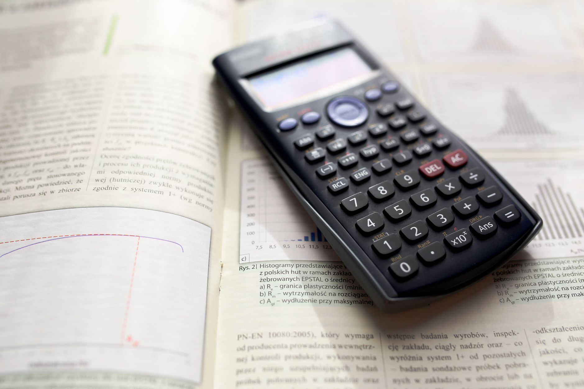 A graphing calculator rests on an open mathematics book with graphs and equations — UPI Study