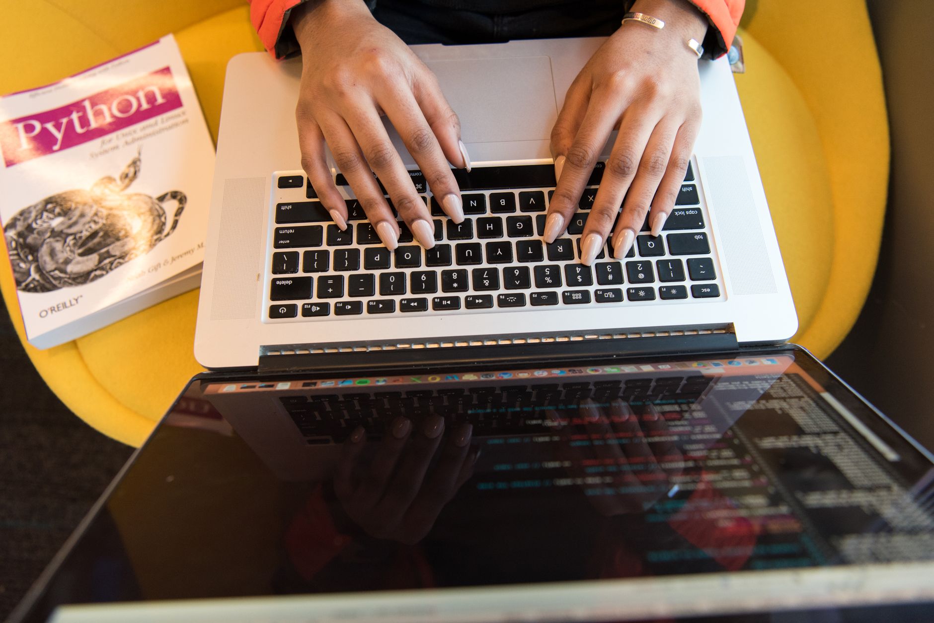 Close-up of hands typing on a laptop keyboard, Python book in sight, coding in progress — UPI Study