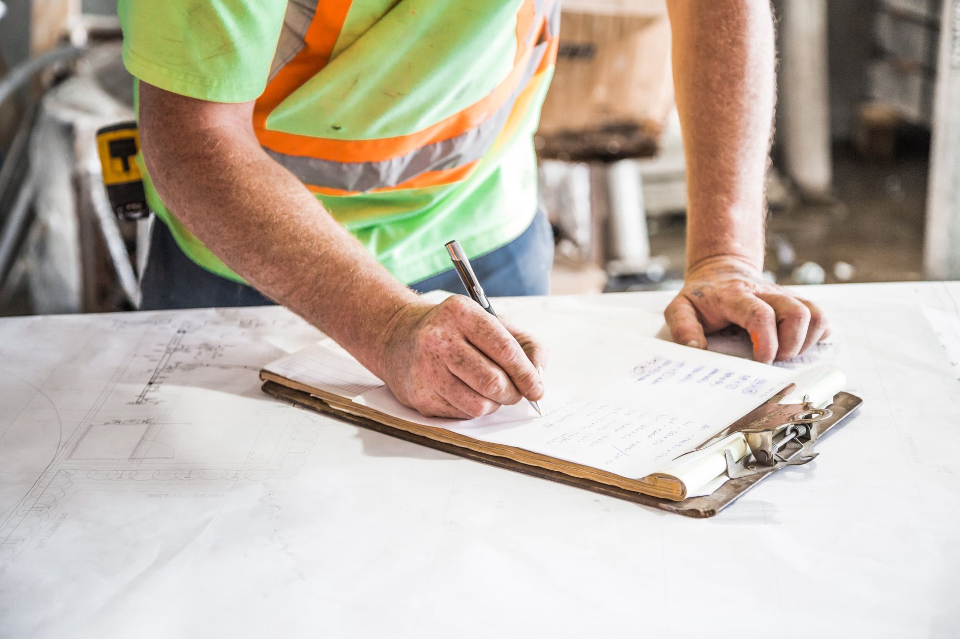A construction worker writes notes on a clipboard at a construction site, emphasizing planning and precision — UPI Study