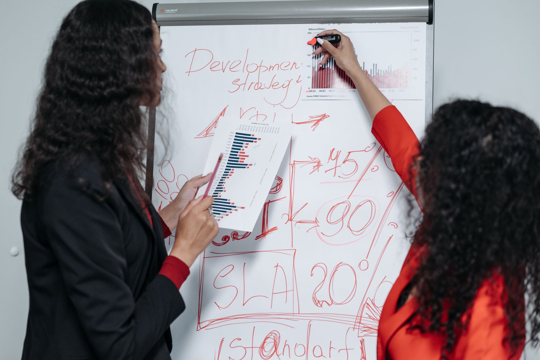 Two professional women discuss and strategize on business development in a modern office setting — UPI Study