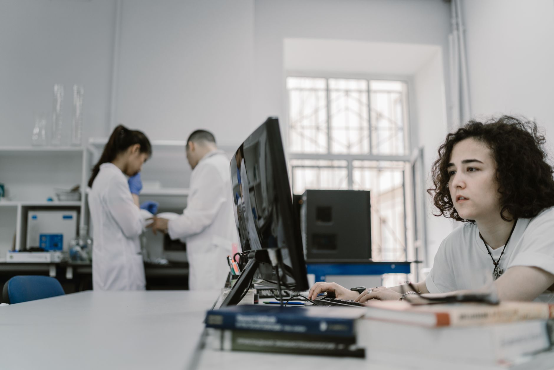 Focused woman working on a computer in a busy laboratory setting, showcasing teamwork and scientific research — UPI Study