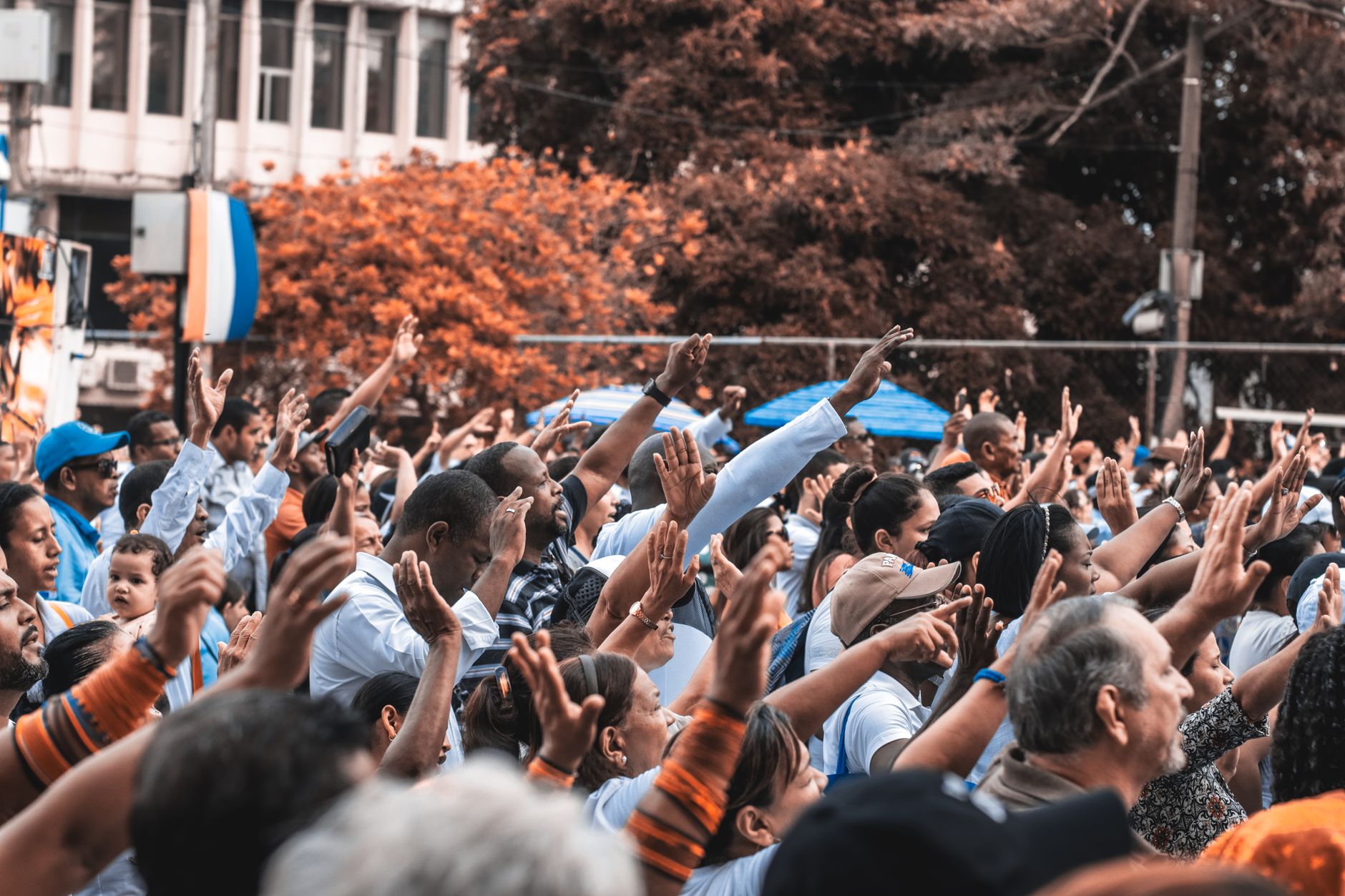 A vibrant outdoor gathering with people raising hands in unity, set in an urban environment — UPI Study