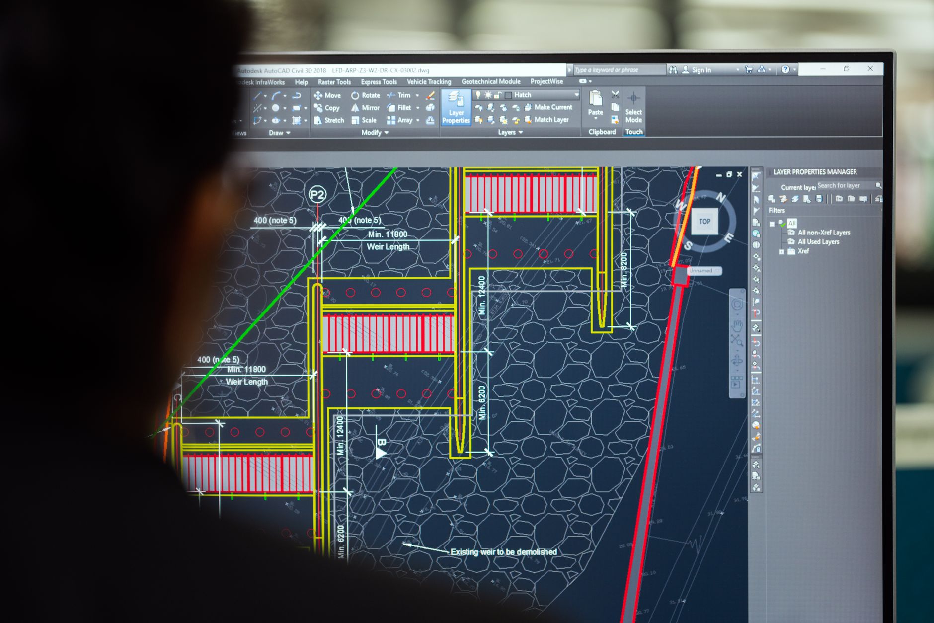 A civil engineer working on a weir design using CAD software on a computer screen in an office setting — UPI Study