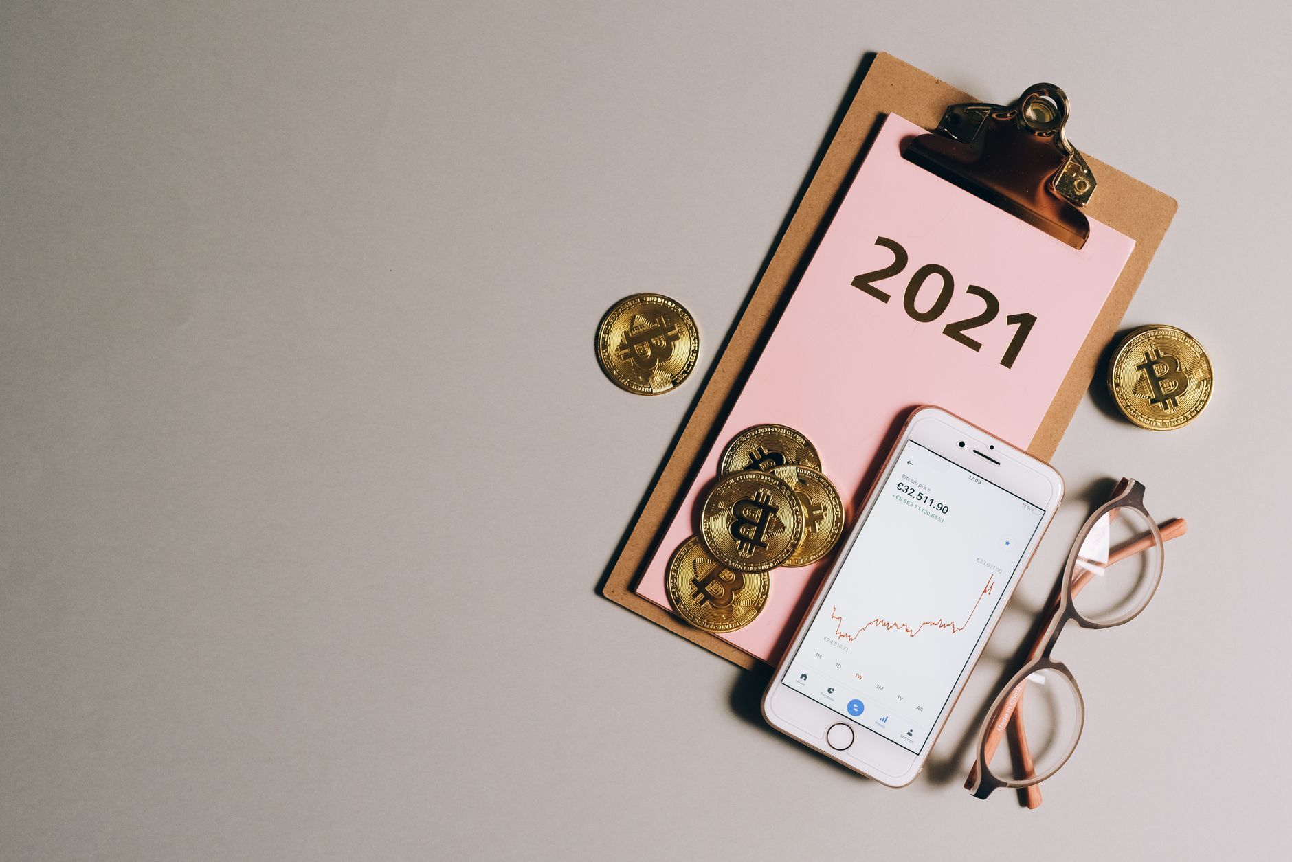 Flat lay of bitcoins, smartphone, eyeglasses, and clipboard with 2021 text, symbolizing cryptocurrency trends — UPI Study