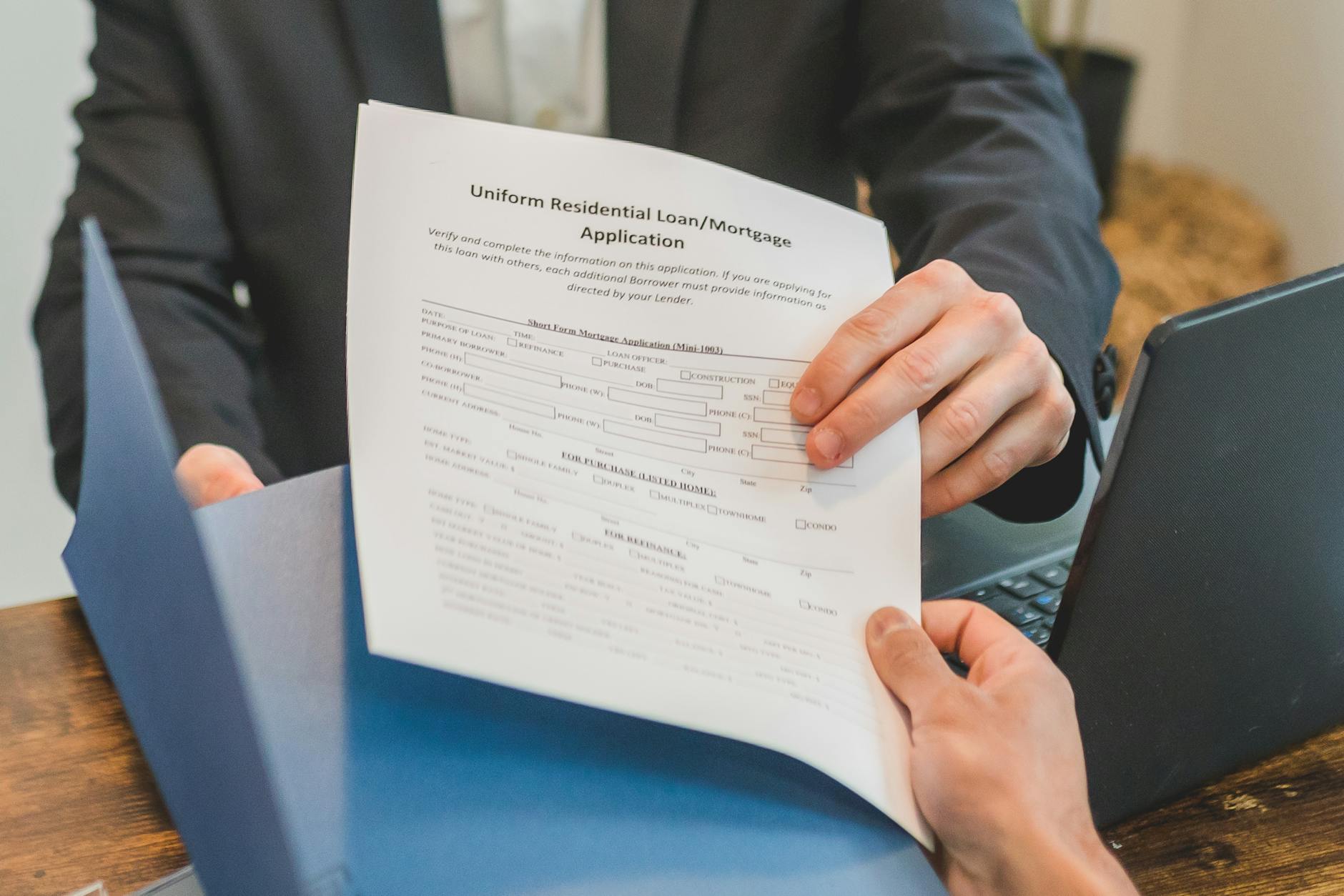Professional setting showing hands exchanging a mortgage application document indoors — UPI Study