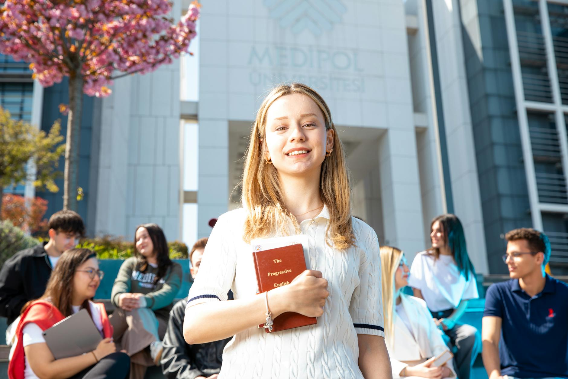 Happy university students socializing on campus, with a focus on a smiling young woman holding a book — UPI Study