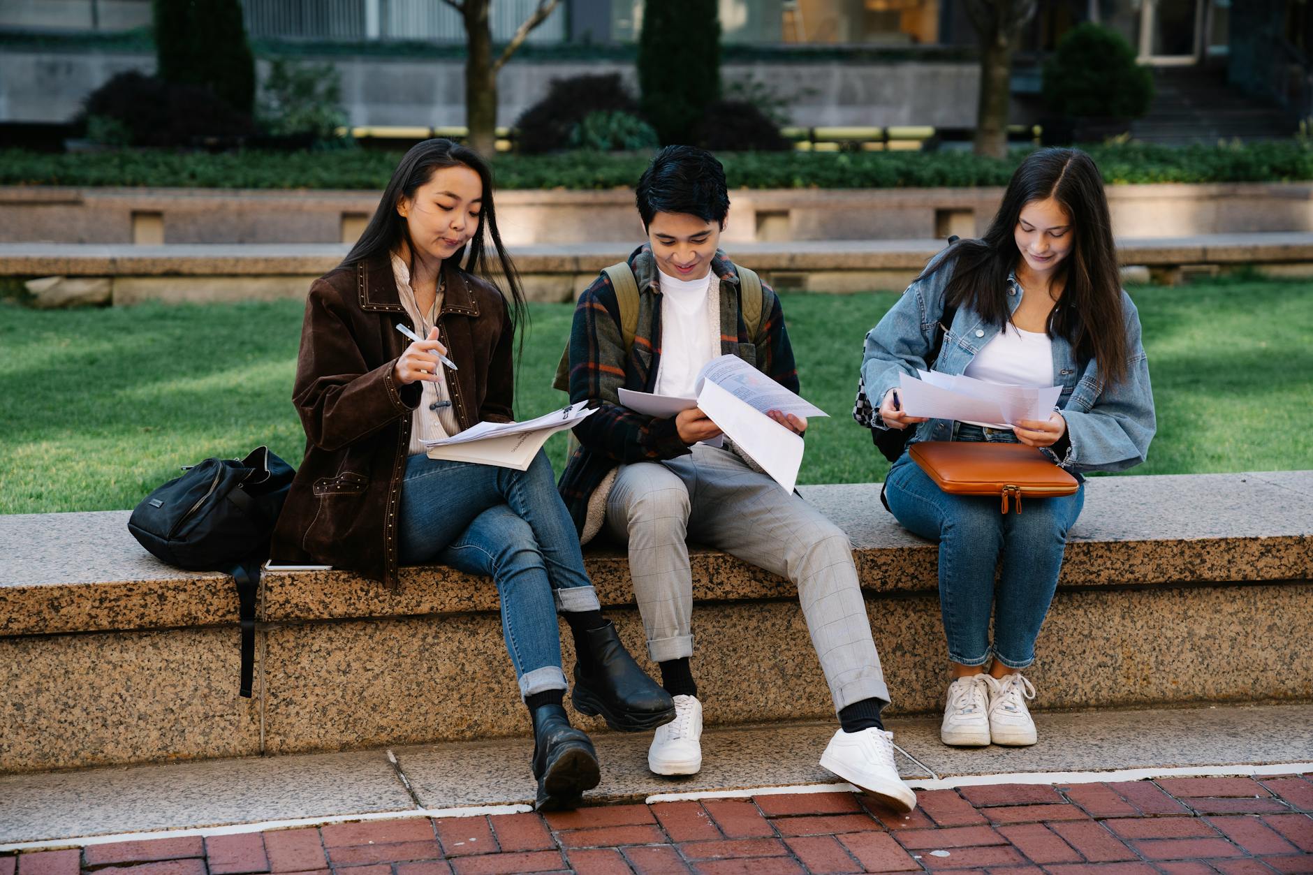 Three students studying together on a bench in a university campus setting outdoors — UPI Study