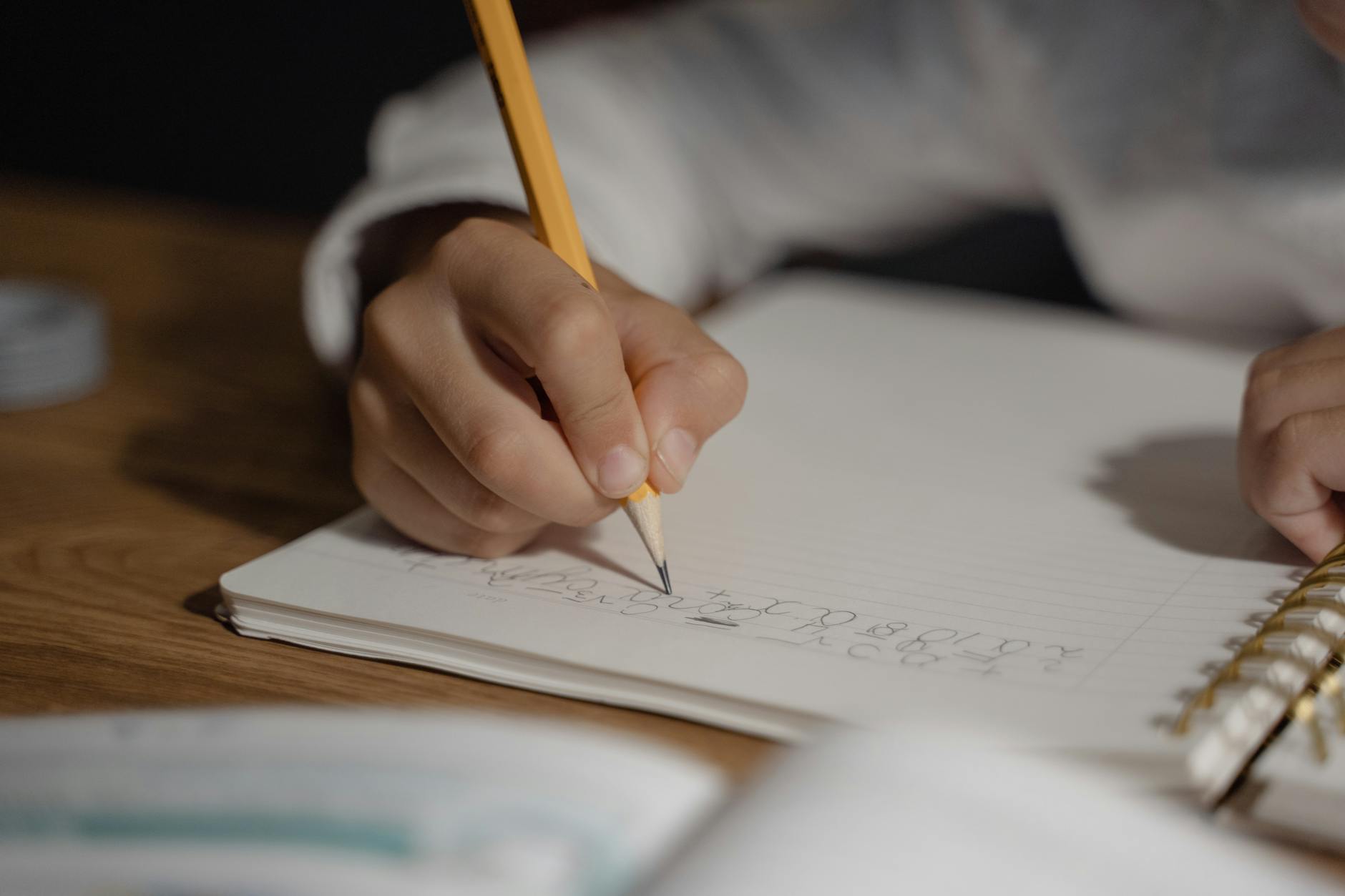 Close-up of a child writing homework using a pencil on a spiral notebook. Ideal for education themes — UPI Study