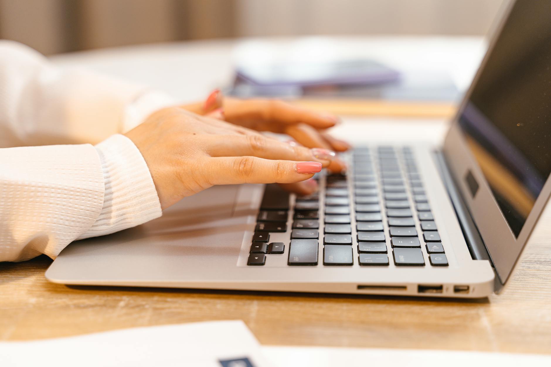 A close-up view of hands typing on a laptop keyboard with a focus on manicured nails and technology — UPI Study